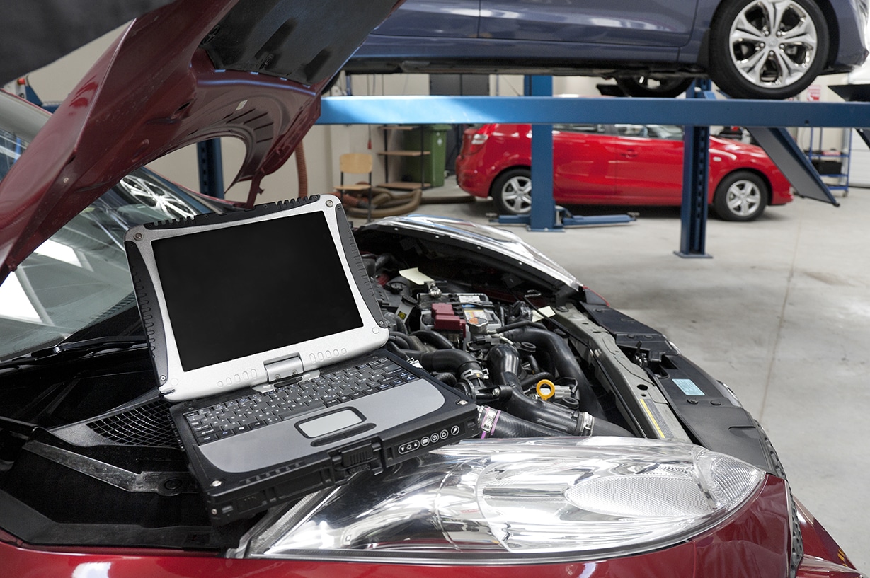 Car in a workshop and a computer running diagnostics on the engine.